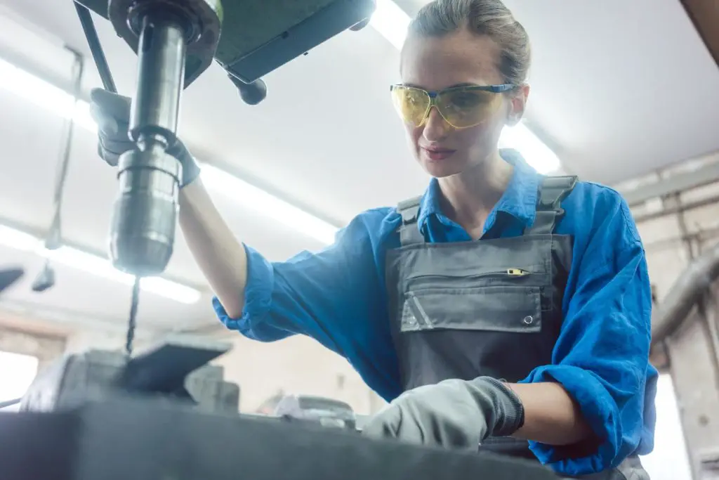 Woman worker in metal workshop using drill